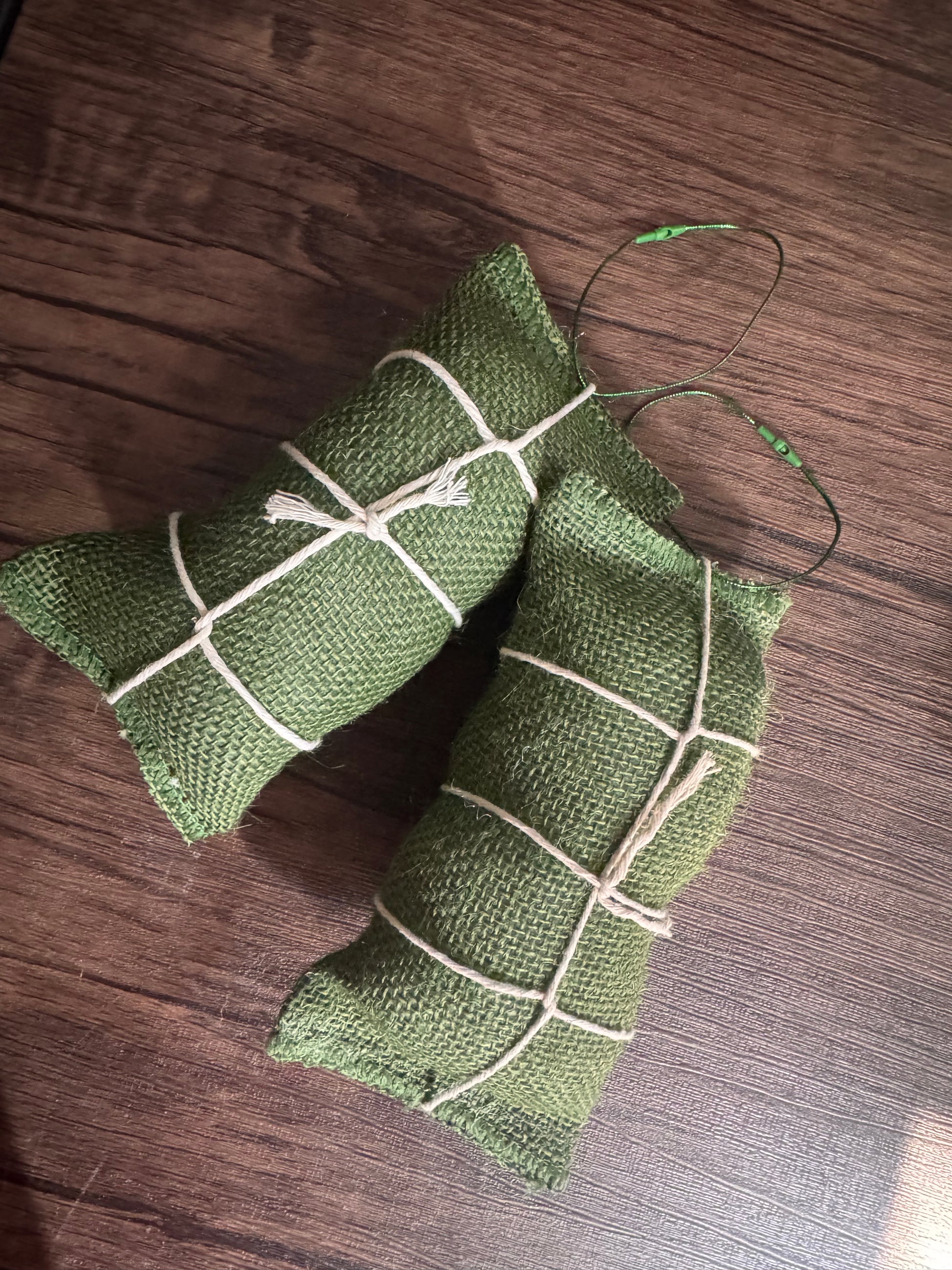 Two green burlap sachets tied with white string, placed on a dark wood surface.